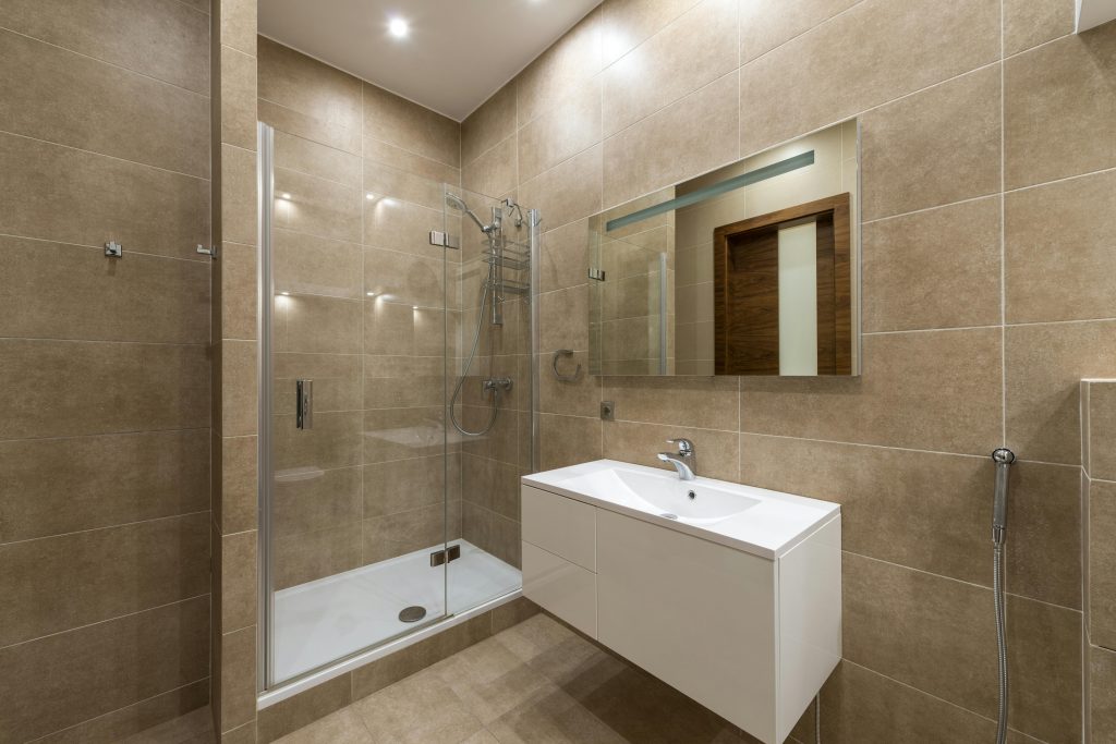 Elegantly designed modern bathroom featuring a glass shower, wall mirror, and large ceramic tiles.